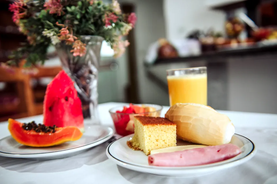 Café da manhã servido: mamão, morango, bolo, pão, frios e suco de laranja
