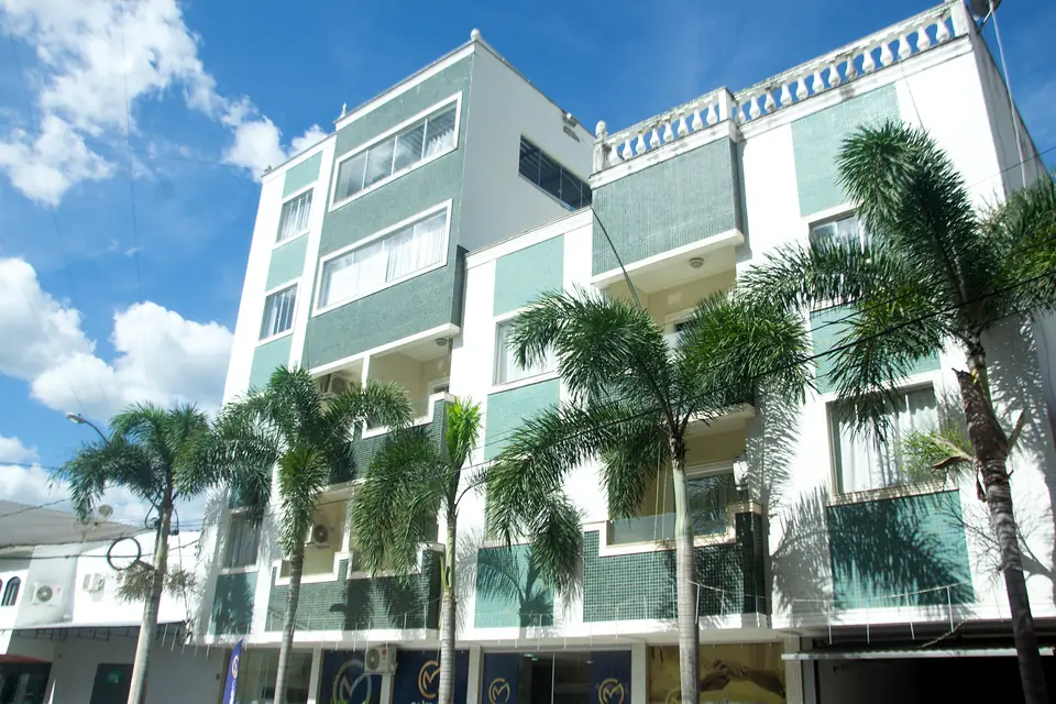 Fachada branca e verde do Italia Palace Hotel com palmeiras e céu azul