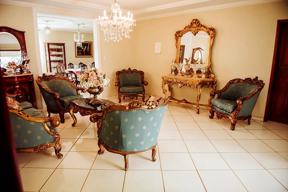 Salão social com lustre de cristal, espelho dourado barroco e poltronas azuis de moldura dourada