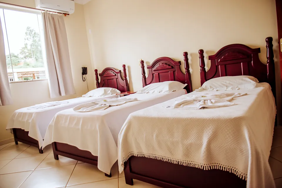Quarto Duplo com duas camas de solteiro de cabeceira vermelha e toalhas dobradas