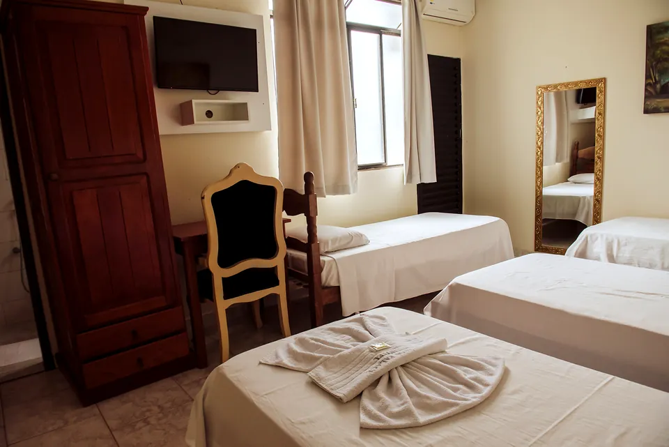 Quarto com três camas de solteiro, guarda-roupa de madeira, televisão e cadeira estofada