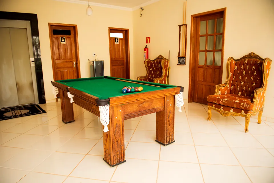 Mesa de sinuca de feltro verde com poltronas de couro capitonê