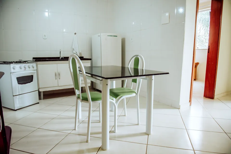 Copa da suíte com geladeira, fogão, mesa de vidro com cadeiras verdes e sofá de couro
